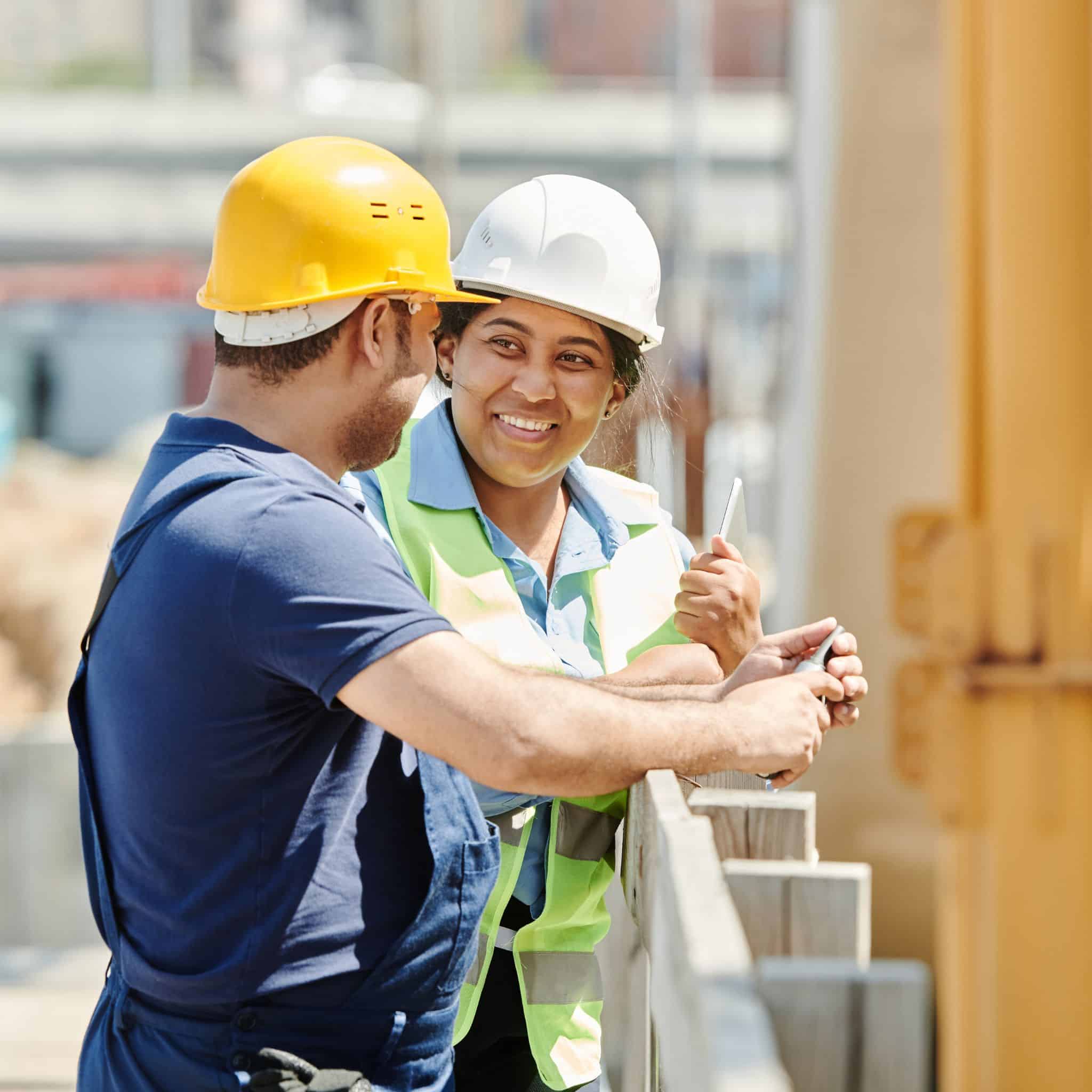 two workers on a construction site talk, one man, one woman