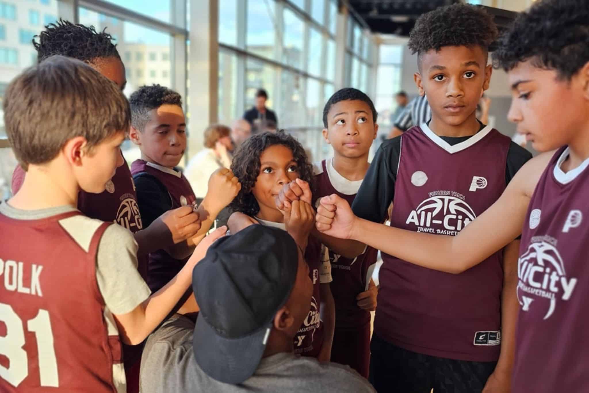 Group of kids fist bumping each other and wearing YMCA "All-City" uniforms