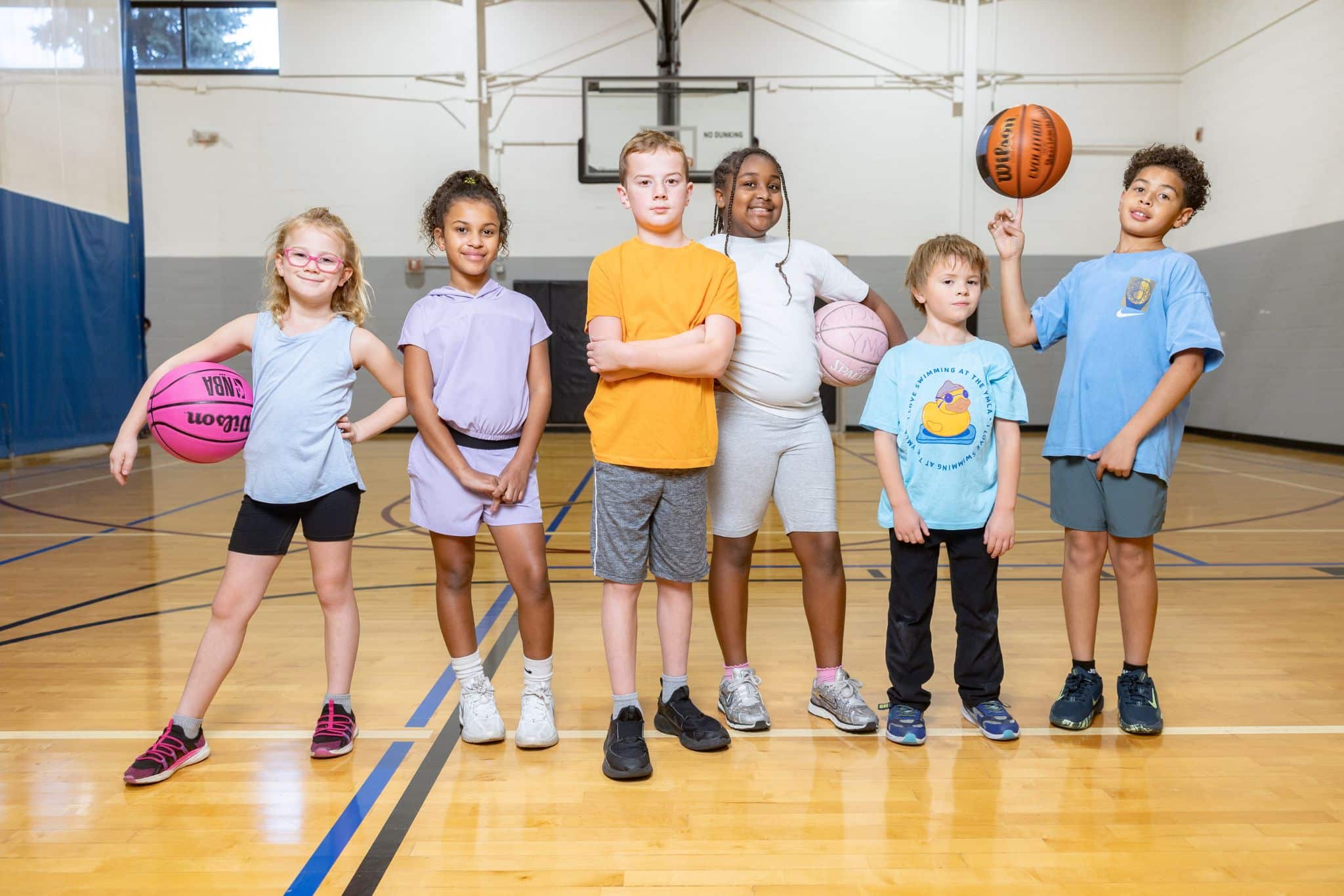 diverse children standing in a row on a basketball court hodling basketballs