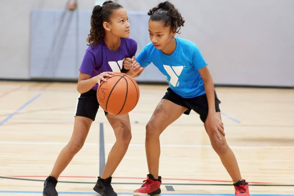 Two girls play basketball in a YMCA basketball league