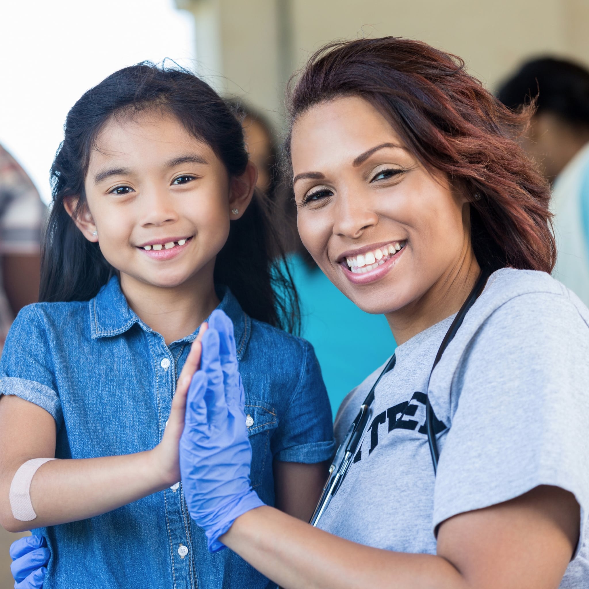 Smiling child with a YMCA staff member wearing medical gloves and a stethoscope at a community health fair.